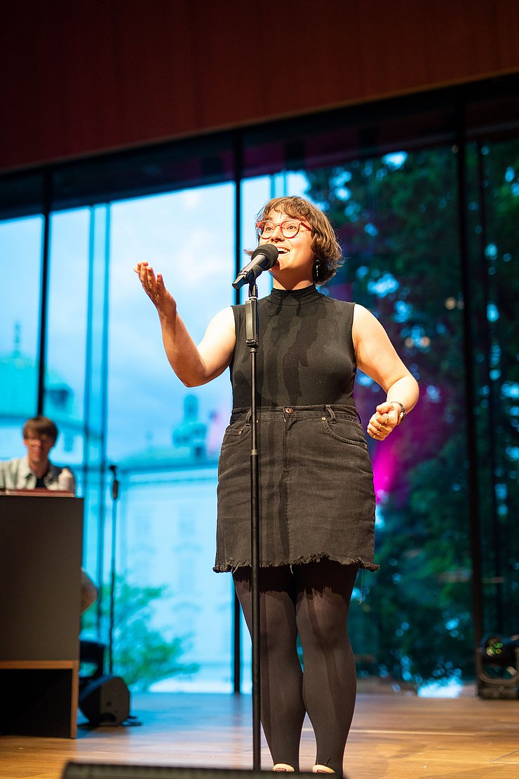 Katrin "ohne H" Rauch steht auf einer Bühne und trägt einen Poetry Slam vor.