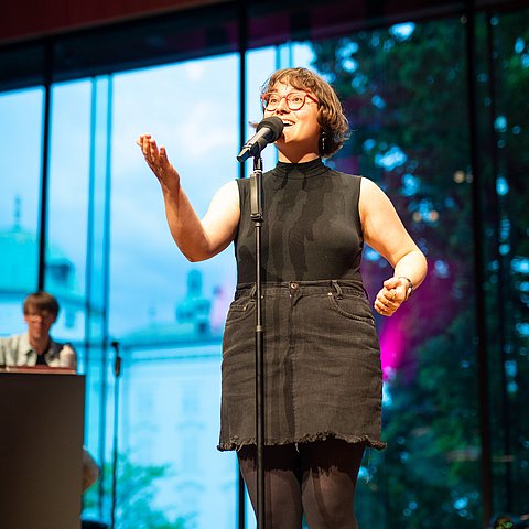 Katrin "ohne H" Rauch steht auf einer Bühne und trägt einen Poetry Slam vor.