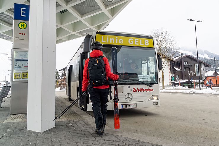 Ein Mann mit Ski in der Hand vor einem Bus an der Haltestelle