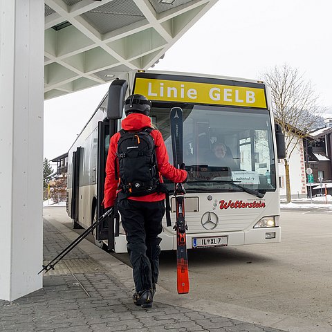 Ein Mann mit Ski in der Hand vor einem Bus an der Haltestelle