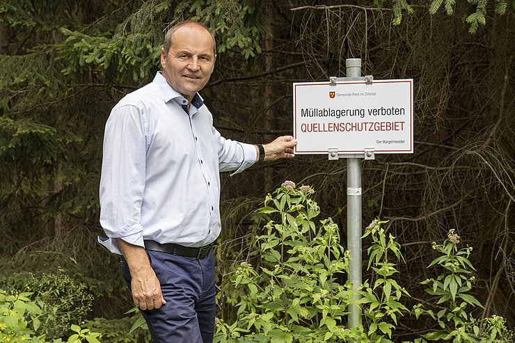 Mann zeigt auf Tafel zu "Müllablagerung verboten, Quellenschutzgebiet"