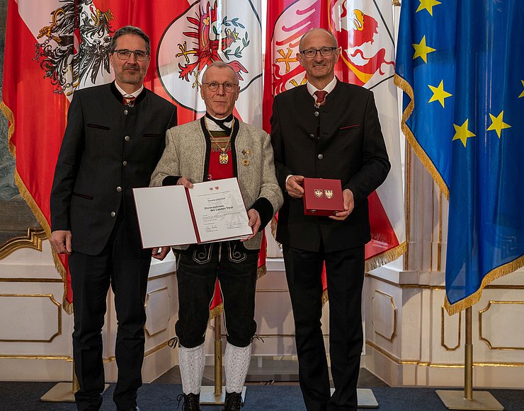 Ausgezeichnet wurde Oswald Gredler, Ehrenobmann des Landestrachtenverbands Tirol, von LH Anton Mattle und LH Arno Kompatscher (li.).