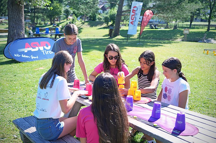 © Land Tirol/Schallhart Mädchen sitzen an Holztisch, spielen mit Bechern, die sie stapeln