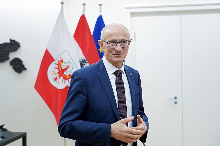 Landeshauptmann Mattle steht vor Fahnen.
