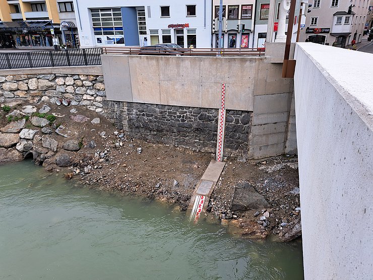 © Land Tirol Flussufer mit Lattenpegel am Rand, der die Wasserhöhe misst.