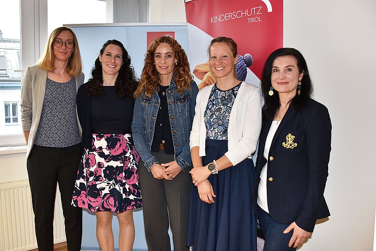 Fünf Frauen stehen vor einem Banner. 