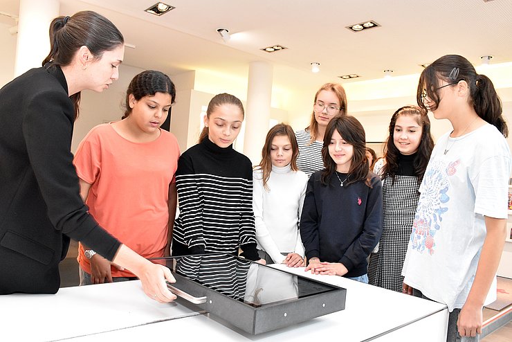 Euregio-Mitarbeiterin Sarah Müller (l.) erklärt Schülerinnen den digitalen „Schlitten“, der Zeitreisen durch Themen und Projekte der Euregio ermöglicht.