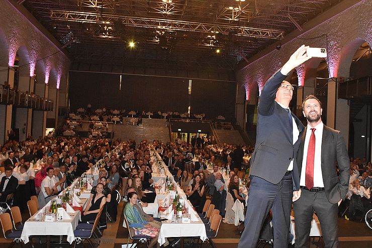 Landeshauptmann Anton Mattle und sein Stellvertreter Georg Dornauer machen ein Selfie im Congress Innsbruck mit den Festgästen im Hintergrund.