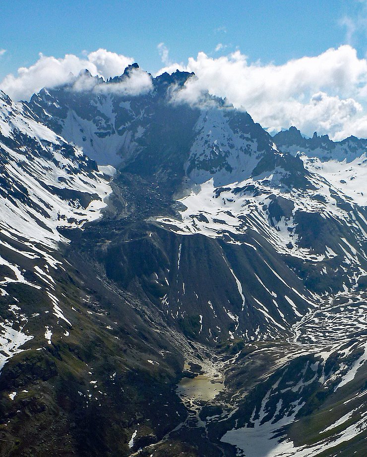 Auf diesem Bild ist der Felssturz aus weiterer Entfernung von vorne zu sehen. Vom Gipfel bis zu einer Senke erstreckt sich die Mure aus Gestein.