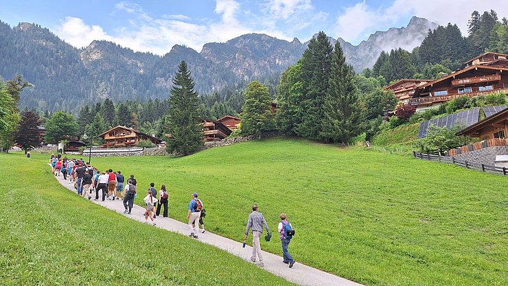 Personen gehen Weg entlang, links und rechts grüne Wiesen
