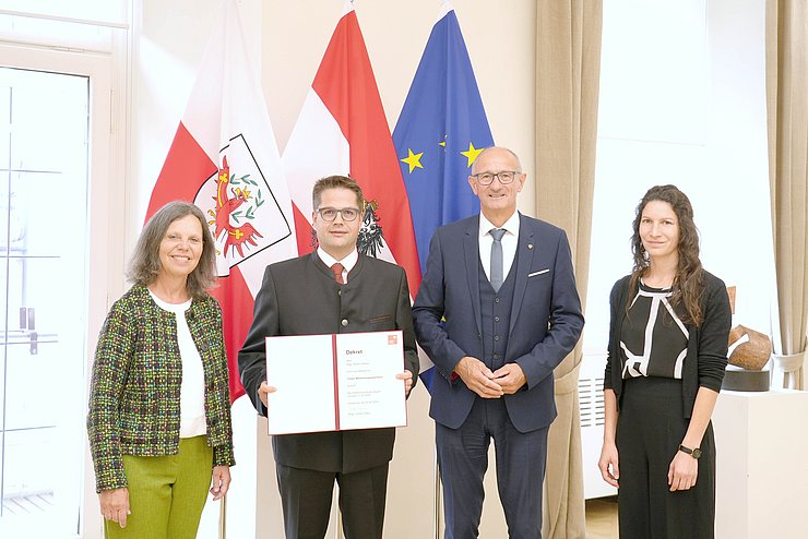 Personen stehen vor Fahnen, Walser hält Dekret