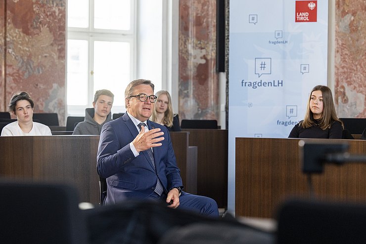 LH Platter sitzt im Landtagssitzungssaal und beantwortet Fragen der SchülerInnen