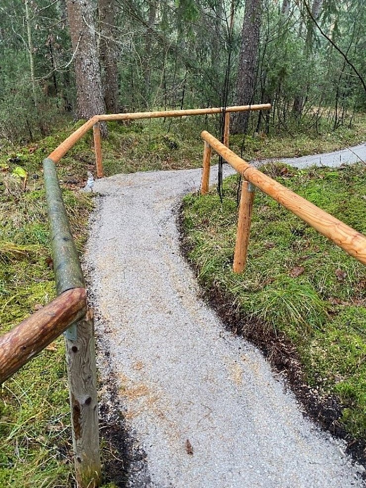 Ein geschotterter Wegabschnitt, der links und rechts von einem Geländer aus Holz begrenzt wird.