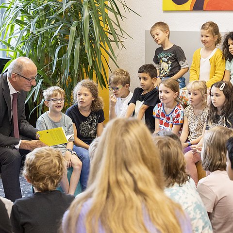 Foto von Landeshauptmann Anton Mattle vor vielen SchülerInnen während er den SchülerInnen aus einem Buch vorliest