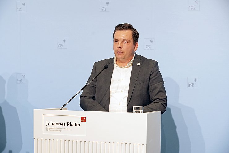 Ein Mann mit kurzen schwarzen Haaren steht an einem Rednerpult.