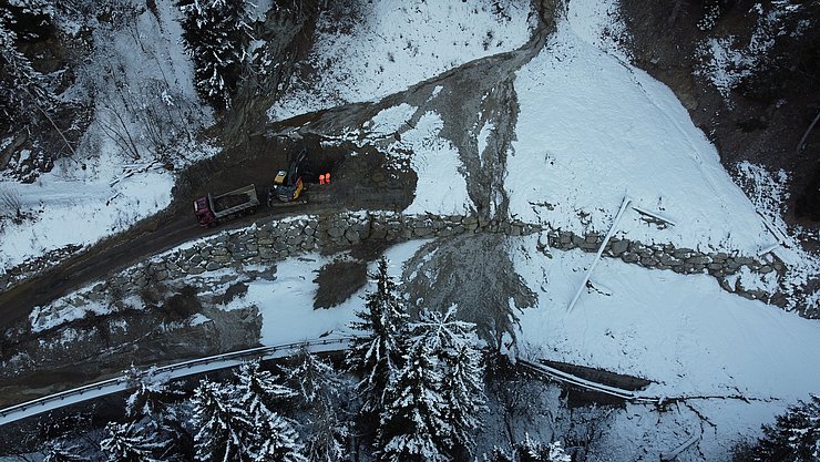 Drohnenaufnahme der B 171: Eine Mure geht über die gesamte Straße und verdeckt diese; ein Bagger steht auf der Mure und schaufelt Material in einen LKW