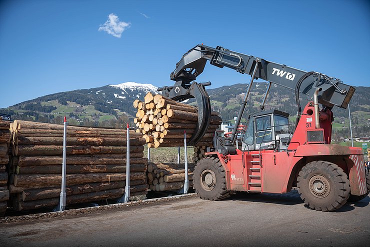 Das mit der Bahn in Jenbach ankommende Rundholz wird auf dem neu errichteten Güterverladeterminal mit einem Verladebagger auf speziell adaptierte Waggons der Zillertalbahn verfrachtet und so zur Verarbeitung nach Fügen transportiert.