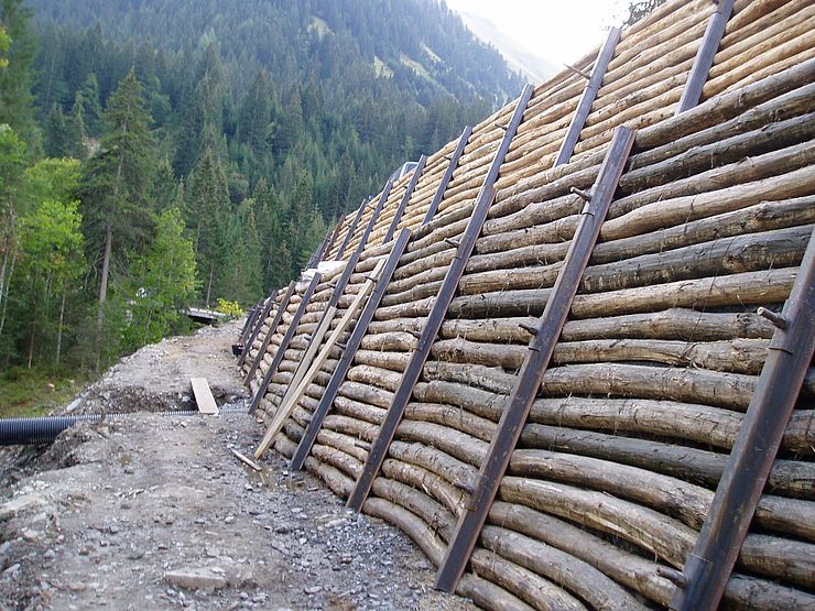 talseitig verankerte Holzstützwand mit begehbarer Berme