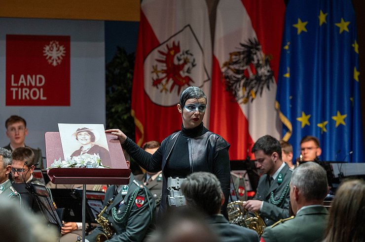 Eine geschminkte Frau zeigt auf ein Porträt.