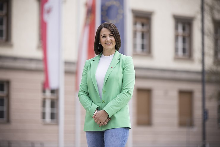 LRin Mair mit grünen Blazer vor dem Landhaus in Innsbruck: Im Hintergrund die Fahnen von Tirol. sterreich und der EU an Fahnenmästen