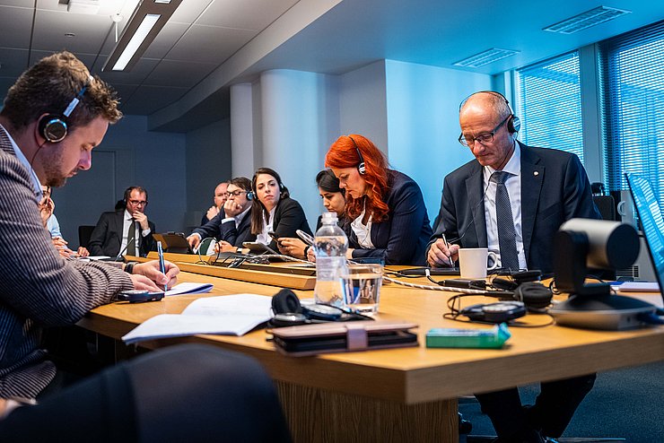 Mattle, Hagele und andere Personen an Tisch sitzend; alle haben Kopfhörer auf