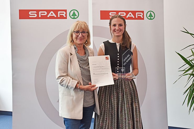 Landesrätin Beate Palfrader mit dem "Lehrling des Monats August 2021" Elisa Taxauer vor einem Spar-Banner