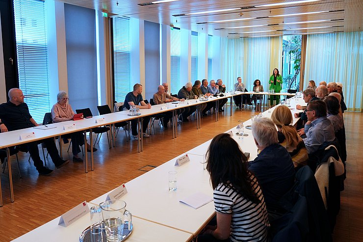 Raum mit vielen Menschen sitzend; Mair stehend und sprechend