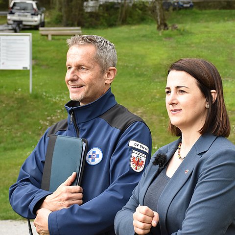 Landesrätin Astrid Mair und Michael Stock von der Wasserrettung Tirol im Freien vor einer Wiese