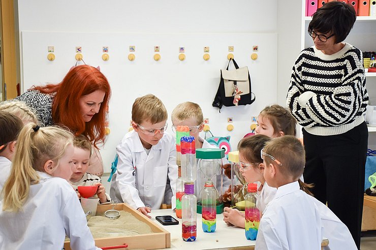 Zwei Frauen und Kinder experimentieren mit bunten Flaschen.