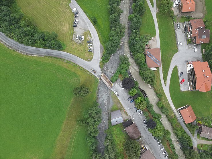 © Land Tirol/Drohnen-Einsatz-Gruppe Blick von oben auf Wildbach, der Straße überflutet. Rechts sind Gebäude und PKWs zu sehen, links ist eine weitere Straße an welcher Autos parken.