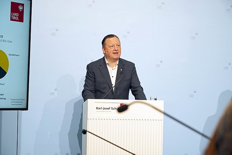 Ein Mann steht an einem Rednerpult, neben ihm ist ein Bildschirm zu sehen. 