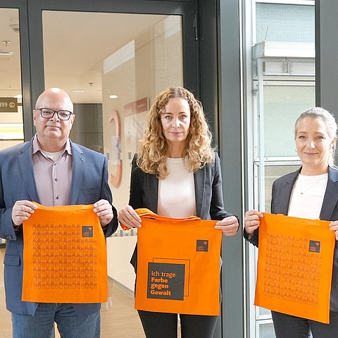 Personen stehen nebeneinander, halten orange Tasche