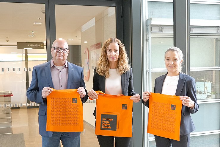 Personen stehen nebeneinander, halten orange Tasche