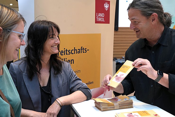 © Land Tirol/Schallhart Mann zwei Frauen Broschüre zeigend