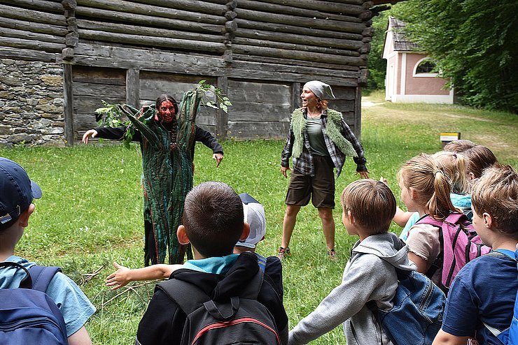 Zwei Märchenfiguren stehen auf einer Wiese und Kinder schauen ihnen beim Schauspielern zu.