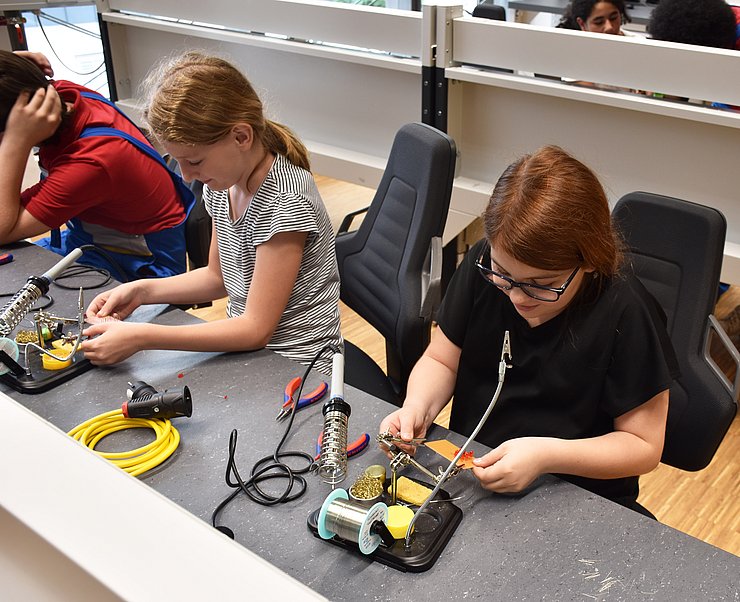 Zwei Schülerinnen arbeiten an einem Werktisch an einem elektrischen Namensschild