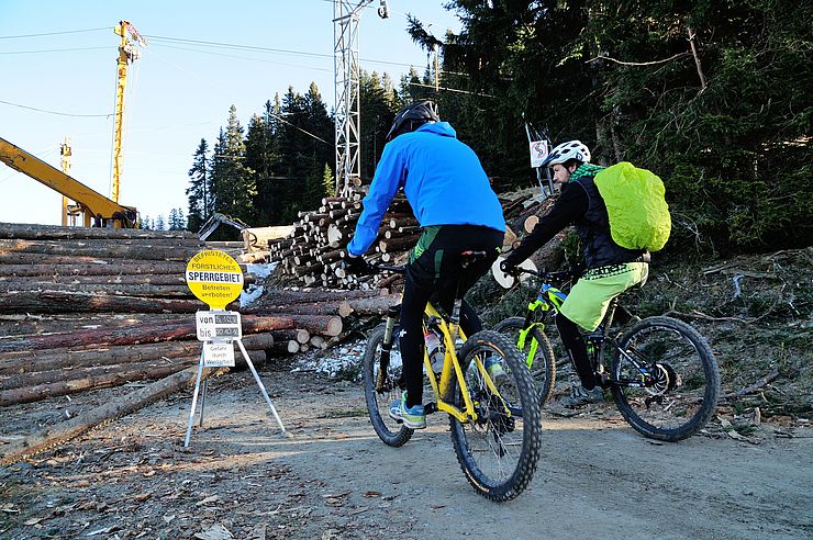 Zwei MountainbikerInnen auf Forstweg; vor ihnen Forstarbeiten und gelbe Sperrtafel