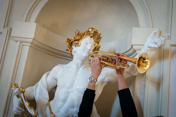 © Land Tirol/Neuner Eine Statue bekommt eine Trompete vor das Gesicht gehalten.