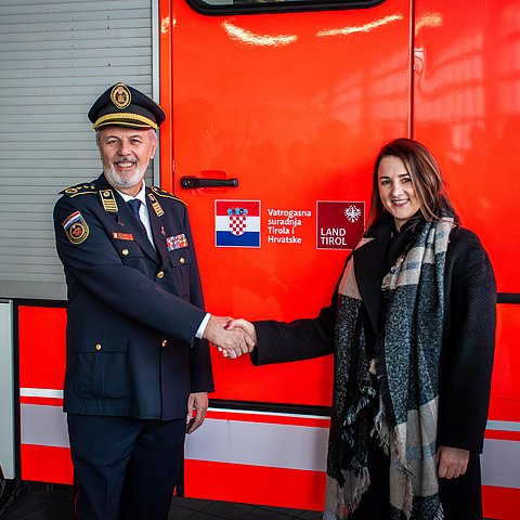 Mair und Sanader stehen vor Feuerwehrauto und geben sich die Hand; auf dem Feuerwehrauto ist das neue Logo zu sehen