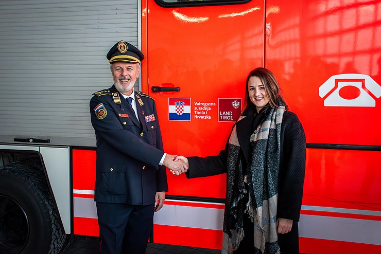 Mair und Sanader stehen vor Feuerwehrauto und geben sich die Hand; auf dem Feuerwehrauto ist das neue Logo zu sehen