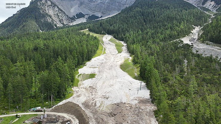 © Land Tirol/Drohnen-Einsatz-Gruppe Blick auf bewaldeten Berghang mit Skipiste (Sommer), welche teils durch Murmaterial bedeckt ist.