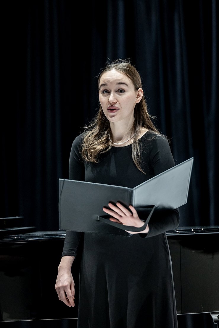 Eine Frau singt und hält eine Mappe.