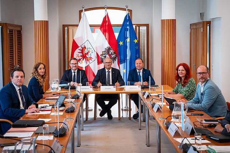© Land Tirol/Fitsch Regierungsmitglieder in Raum vor Fahnen an Tisch sitzend