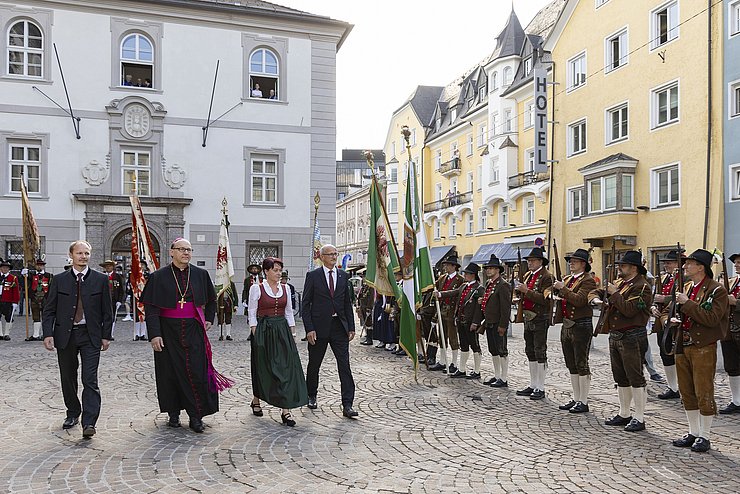 Schützen stehen in der Reihe mit Gewehr, vier Menschen gehen an ihnen vorbei