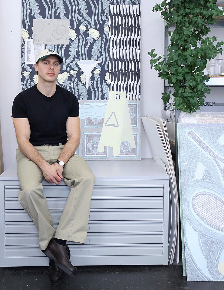 Ein junger Mann mit Kappe sitzt vor einem Bild.