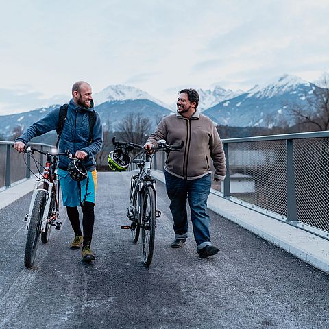 Winkler und Grißmann mit Rädern über Brücke gehend