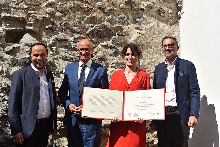 Gruppenfoto vor einer alten Steinmauer; Mairer mit Urkunde in ihren Händen