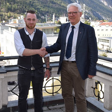 Zwei Männer auf Balkon schütteln sich die Hand