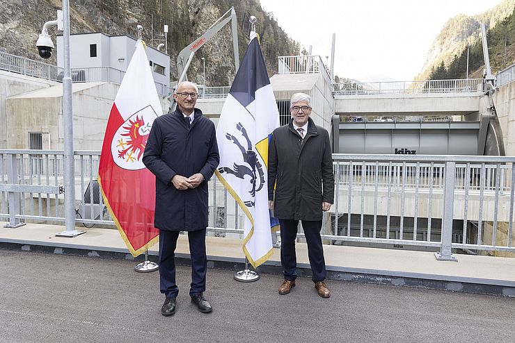 Zwei Personen vor den Flaggen Tirols und Graubündens.