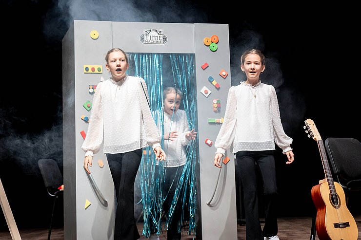 Drei Mädchen vor einer selbstgebastelten Maschine.